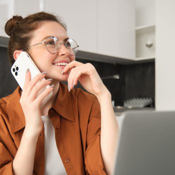 Portrait of woman working from home with laptop, making a phone call, using smartphone, looking thoughtful, order something online.
